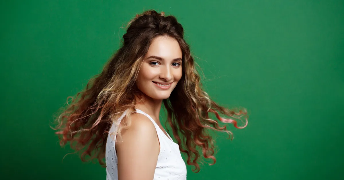 Woman with wavy brunette hair smiling on green background, hair color ideas for dark hair fresh tone